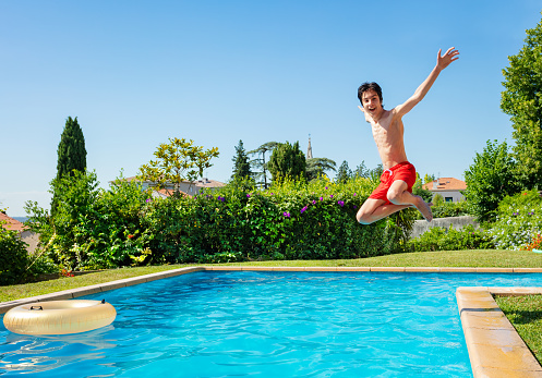 Teenage boy jump in mid air into the swimming pool view from side scream and smile