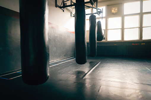 Black heavy bags in an empty gym with a lot of sunlight.