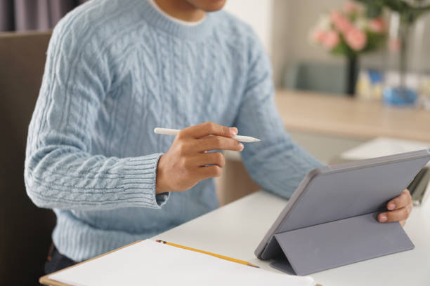 istock asian young student man entrepreneur working with tablet studying learning online at home. e-learning webinar meeting. social distance in covid pandemic 1303404373