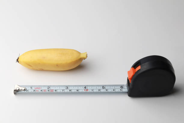 Small banana with measuring tape on a white background Close up a small yellow banana with measuring tape on a white background little banana stock pictures, royalty-free photos & images