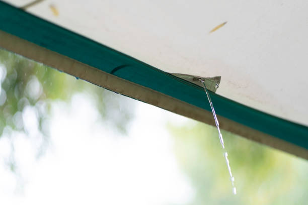 Rain water pours through an awning eyelet on a tent in a camping ground in summer in New Zealand. A pool of water has formed on the roof of the awning and is draining through the eyelet as the rain continues.