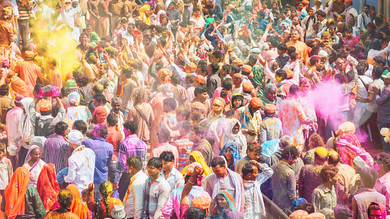 Large crowd of indian people covered with colorful face powder partying and celebrating the famous Holi Festival in India. Panorama Shot. Holi Festival in Barsana, Rajasthan, India, Asia.