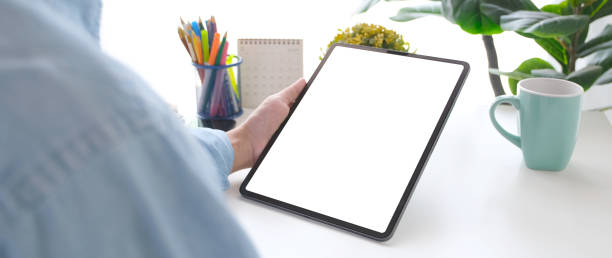 istock Close up of man hand holding digital tablet with blank screen on working table background for mock up, template 1303421385