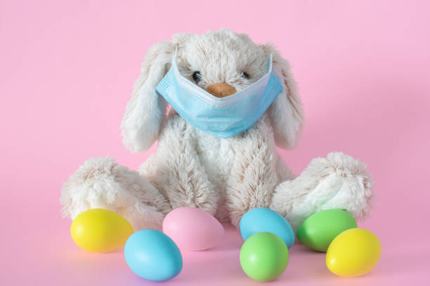 istock Easter bunny in protective face mask and colored eggs on pink background. Ester holiday during corona virus concept. 1303426162