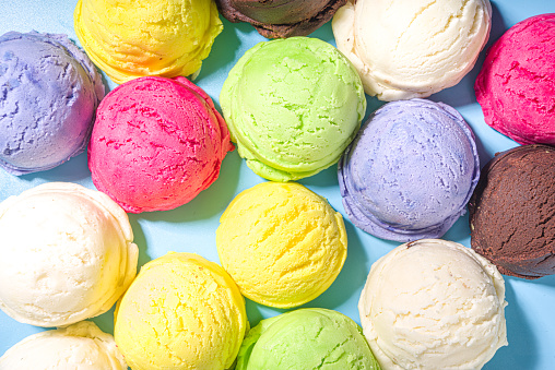 Colorful various ice cream scoops pattern on pastel blue background. Summer minimalism pattern flat lay with hard light. Chocolate vanilla blueberry strawberry pistachio orange ice-cream balls top view