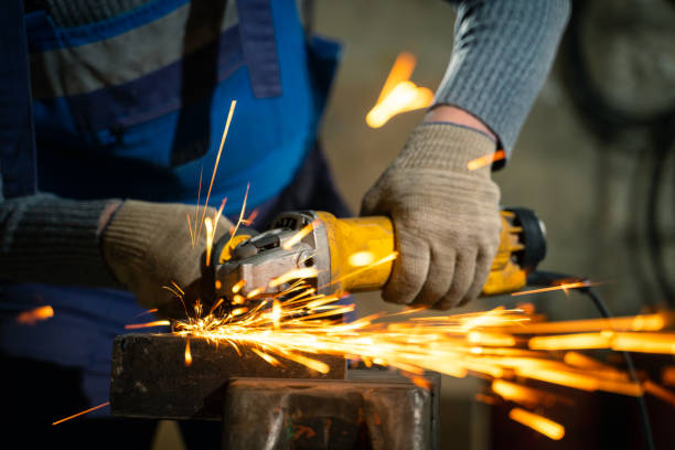 istock Locksmith in special clothes and goggles works in production. Metal processing with angle grinder. Sparks in metalworking 1303439505