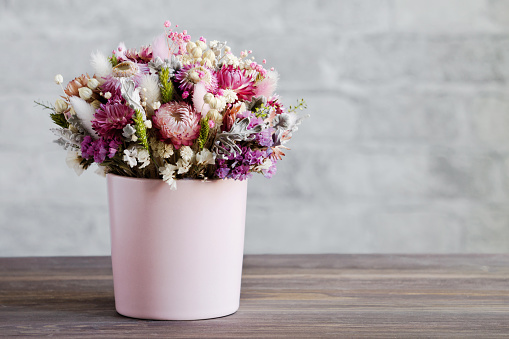 Un delicado ramo de flores secas en un jarrón rosa. Superficie de madera, pared de ladrillo. Primer plano, espacio de copia. El concepto de una tarjeta de felicitación suave en colores pastel photo