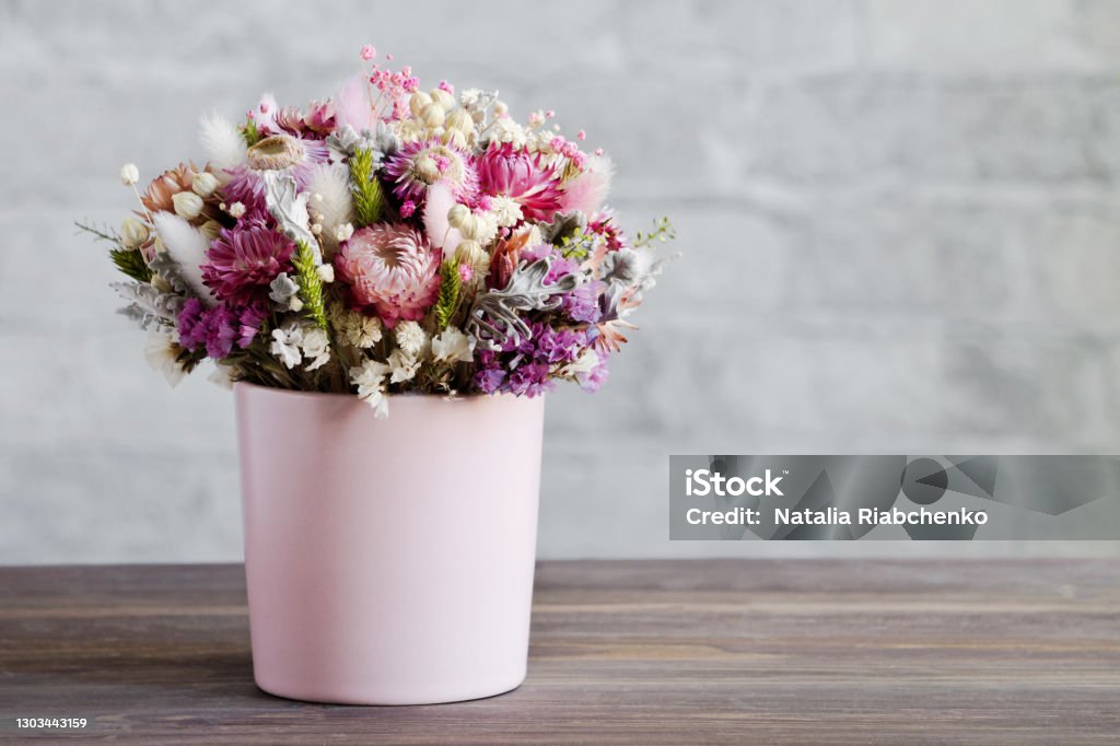 A delicate bouquet of dried flowers in a pink vase. Wooden surface, brick wall. Close-up, copy space. The concept of a gentle greeting card in pastel colors A delicate bouquet of dried flowers in a pink vase. Wooden surface, brick wall. Close-up, copy space. The concept of a gentle greeting card in pastel colors. Bouquet Stock Photo