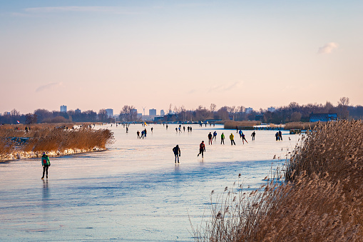 Ice skating on the Braassemermeer near Roelofarendsveen in the municipality of Kaag en Braassem mede Veendermolen on a sunny day. It is mid-February 2021 in the Netherlands, people are skating on a large lake.