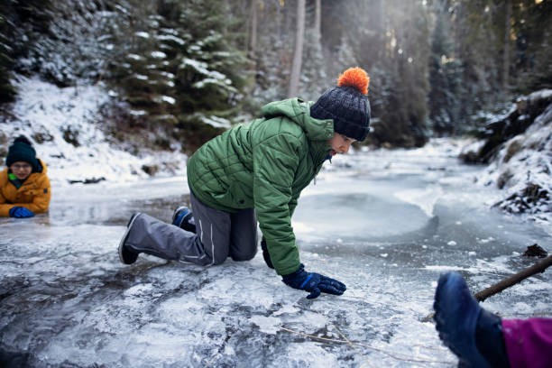 Kids enjoying cold winter day in the winter forest. Teenage girl and her brother playing on the frozen mountain stream.\nShot with Canon R5