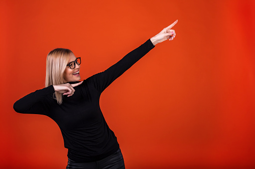 Excited Young Woman Pointing Upwards while standing in red studio.