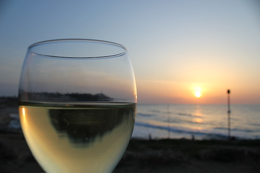A glass of white wine in front of the setting sun over the Mediterranean Sea. Aperitif - cheers