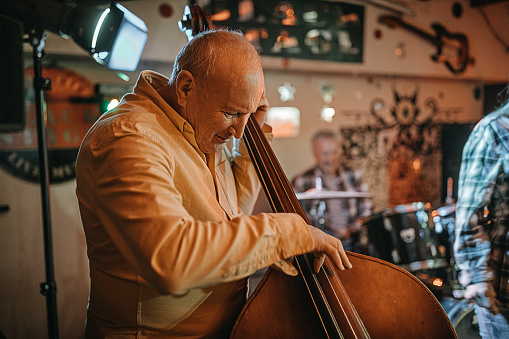 Senior man play contrabass with his band in the club for friends