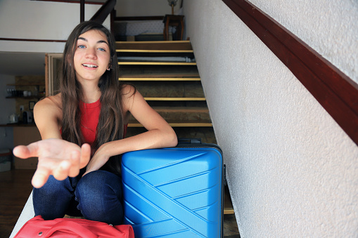 Happy teenage girl sitting around suitcases