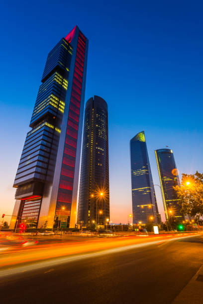 Futuristic neon skyscrapers overlooking zooming traffic Cuatro Torres Madrid Spain The futuristic skyscrapers of the Cuatro Torres Business Area illuminated at sunset above the traffic zooming along the rush hour highway below in Madrid, Spain's vibrant capital city. contemporary madrid european culture travel destinations stock pictures, royalty-free photos & images