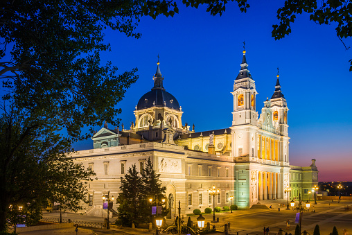 The ornate domes and spires of the Almundena Cathedral spotlit against the deep blue skies of sunset in the heart of Madrid, Spain's vibrant capital city.