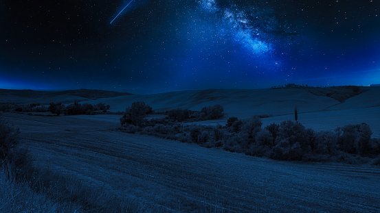 The beautiful Tuscany in Italy under the blue starry nightsky with a shooting star