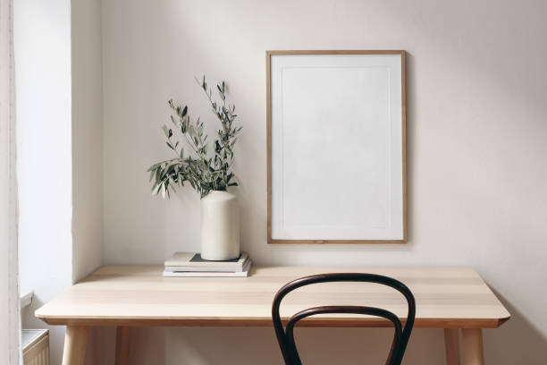 istock Home office concept. Old books, empty vertical wooden picture frame mockup hanging on white wall. Wooden desk, table. Vase with olive branches. Elegant working space. Scandinavian interior design. 1303452861