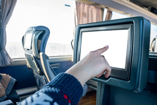 The interior of the bus with an interactive touch screen, a woman's hand touches the screen installed on the seat in a long-distance bus.