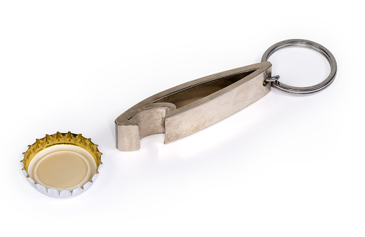 Metal bottle opener in the form of a keychain with attached steel split ring and inverted used metal crown bottle cap with plastic backing close-up on a white background