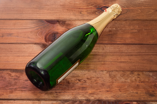 Green sealed bottle of sparkling wine lies on an old wooden rustic table