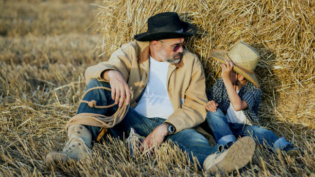 Cowboys Father and son resting in the field wear hats, shirts and jeans wheat ranch stock pictures, royalty-free photos & images