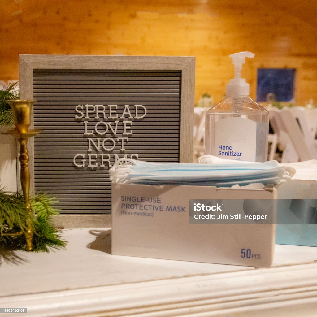 Spread Love Not Germs Sign at a Wedding Reception A sign has a quote about spreading love not germs. There is a box of single use face masks and a bottle of hand sanitizer Hand Sanitizer Stock Photo