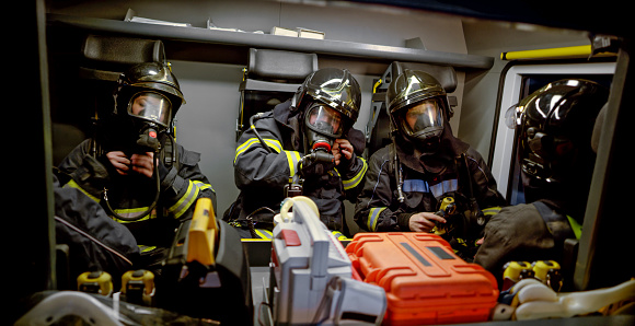 Group of firefighters wearing gas masks while sitting together in fire engine.