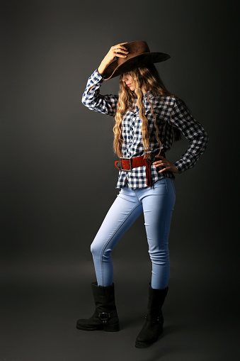 cowboy girl in a hat with a rope on a dark background. Stylish cowboy in jeans and hat.