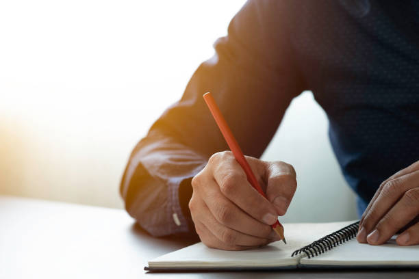 istock Close-up of man hand using writing pencil memo on notebook paper or letter, diary on table desk office. Workplace for student, writer with copy space. business working and learning education concept. 1303465932