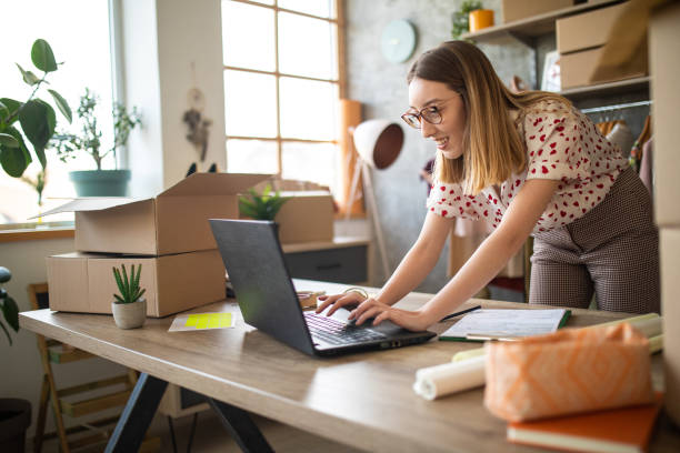 Young female entrepreneur receiving new orders in her e-commerce clothing shop Young female entrepreneur receiving new orders in her e-commerce clothing shop market vendor stock pictures, royalty-free photos & images