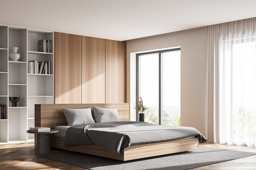 Corner of stylish master bedroom with white and wooden walls, wooden floor, comfortable king size bed, a bookcase and windows with blurry view. 3d rendering