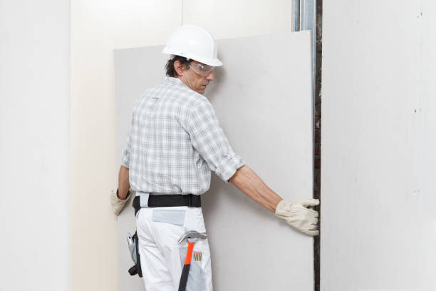 istock man drywall worker installing plasterboard sheet to wall. Wearing hardhat, work gloves, safety glasses and tool belt. Isolated on white background with copy space 1303467892