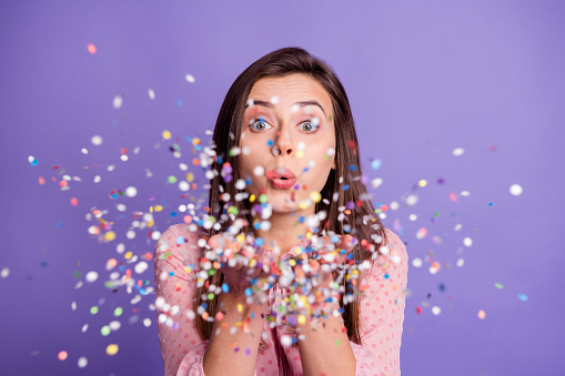 Photo of young attractive girl blow serpentine confetti you celebration party isolated over purple color background.