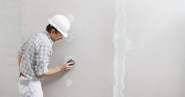 man drywall worker or plasterer sanding and smoothing a plasterboard walls with stucco using a sandpaper holder. wearing white hardhat and safety glasses. panoramic image with copy space - plasterer construction site manual worker plaster imagens e fotografias de stock