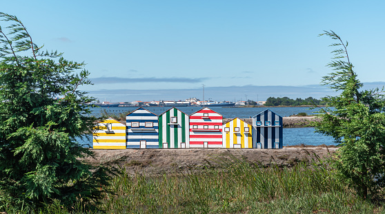 Small houses of primary colours, yellow, green, blue and red striped, typical of a portuguese seaside village in the afternoon on a sea in the afternoon