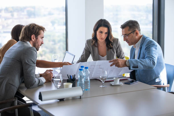 Four business people in a meeting at conference table, analyzing plan on spreadsheet