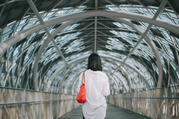 rückansicht asiatische chinesische mittlere erwachsene frau im freien mit schützenden gesichtsmaske an der fußgängerbrücke - women rear view one person arch stock-fotos und bilder