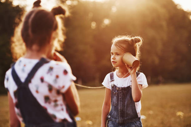 istock Two female kids stands in the field and talking by using string can phone 1303474563