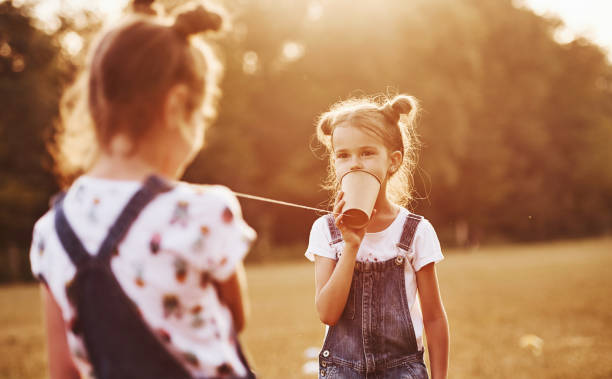 istock Two female kids stands in the field and talking by using string can phone 1303474765