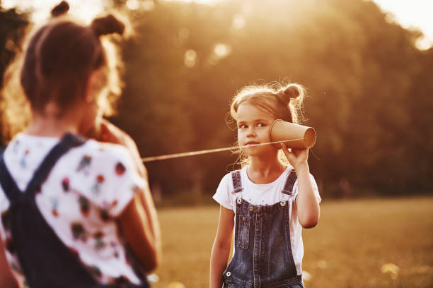 Two female kids stands in the field and talking by using string can phone stock photo