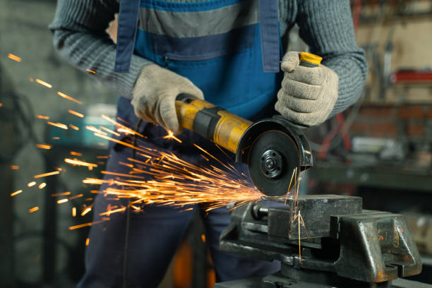 istock Locksmith in special clothes and goggles works in production. Metal processing with angle grinder. Sparks in metalworking 1303475076