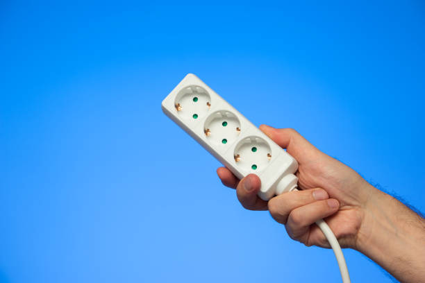 istock Electrical extension cord with multiple plug sockets held in hand by Caucasian male hand isolated on blue 1303476552