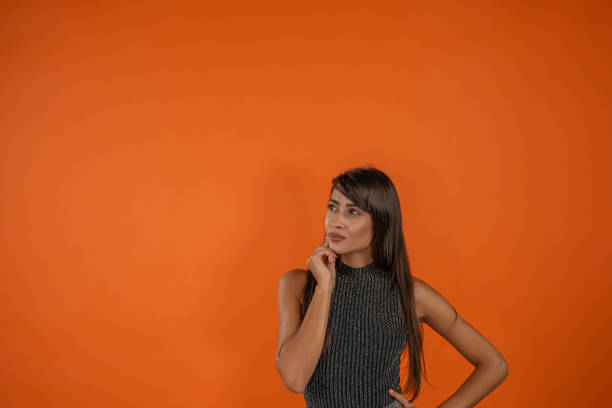 istock Thoughtful  brunette with grey dress looking at blank text space, orange background. Concept of shopping, summer sale 1303479650