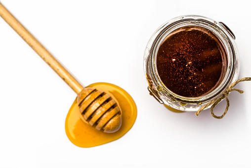 Drop of honey, dipper and glass jar of honey on white background, overhead