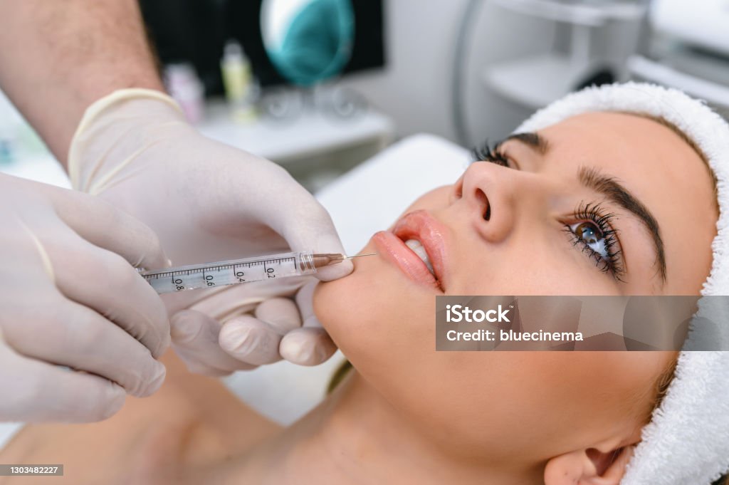 Beauty treatment with Botox The doctor cosmetologist makes the Rejuvenating facial injections procedure for tightening and smoothing wrinkles on the face skin of a beautiful, young woman in a beauty salon. The hands of cosmetologist are close-ups that inject hyaluronic acid into the lips of the woman. Dermal Filler Stock Photo