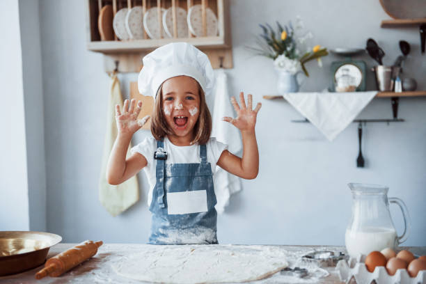 istock Having fun. Cute kid in white chef uniform preparing food on the kitchen 1303482306