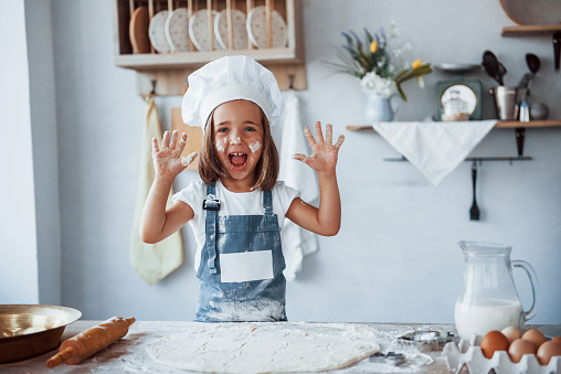 Having fun. Cute kid in white chef uniform preparing food on the kitchen.