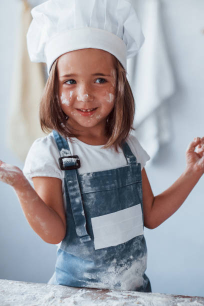 istock Having fun. Cute kid in white chef uniform preparing food on the kitchen 1303482453