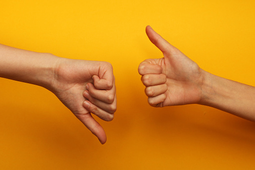 Two hands on a yellow background, one of them is with thumb up and other is with thumb down